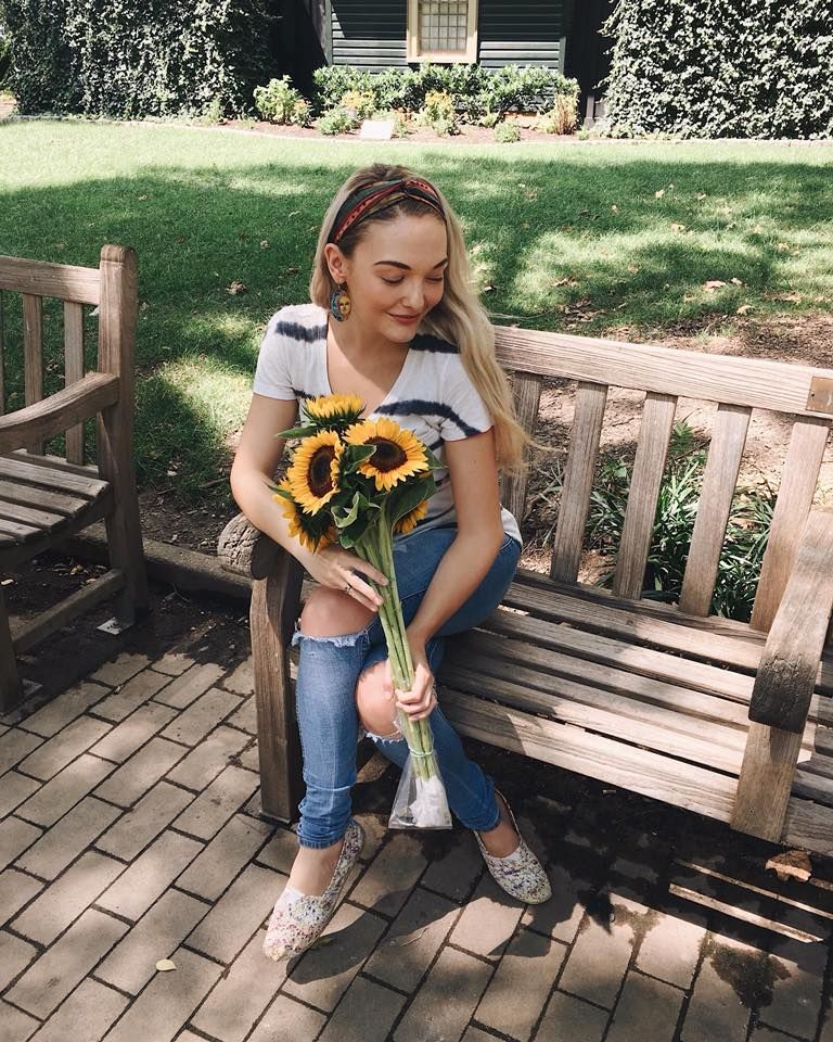 Miranda M. sitting on a bench holding a bouquet of sunflowers
