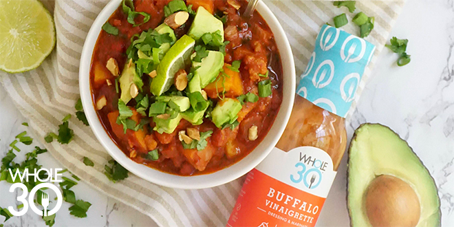 A bowl of buffalo chicken chili, next to a bottle of Whole30 Buffalo Vinaigrette dressing and marinade. In the bottom left corner is a white Whole30 logo.