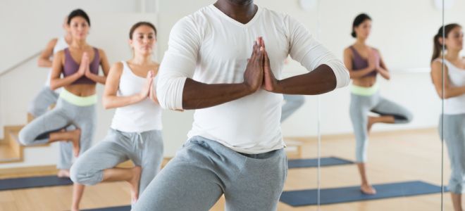 A diverse group of people practices tree pose in a yoga class