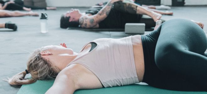 Two women lay on yoga mats and twist their left leg over their right