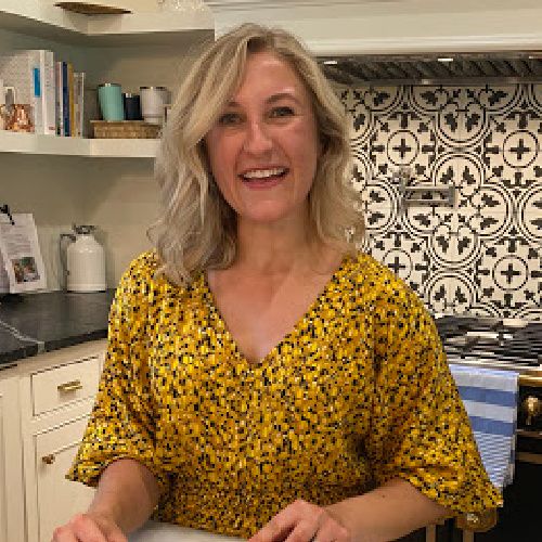 Whitney stands in the kitchen and smiles at the camera.