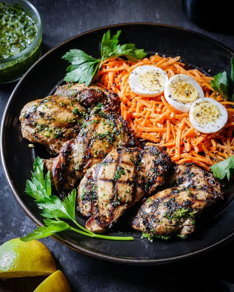 A delicious bowl of chimichurri chicken, paired with a side of sliced carrots and seasoned hard boiled eggs.