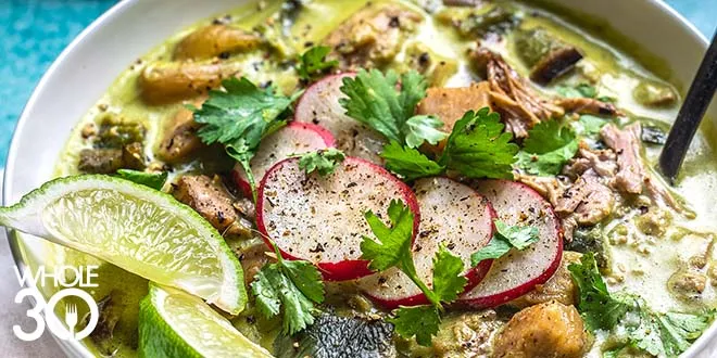 Tender Whole30 Pork Posole in a bowl with sliced lime