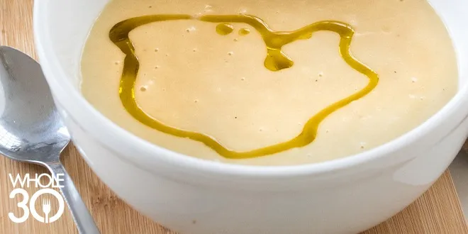 A big bowl of creamt Whole30 Roasted Garlic Soup drizzled with an olive oil drizzle