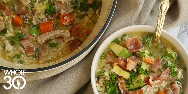 Chicken and vegetable soup in a large bowl, next to a small bowl of the same soup with a golden spoon