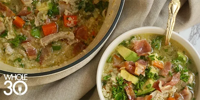 Chicken and vegetable soup in a large bowl, next to a small bowl of the same soup with a golden spoon