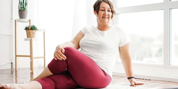 Woman sits on yoga mat with one leg over the other and is twisting her body to the side.