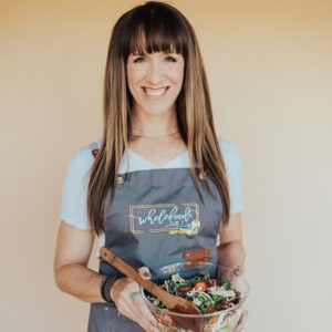 Digital Content Producer, Autumn Michaelis wearing an apron and holding a bowl of fresh salad smiling at the camera.