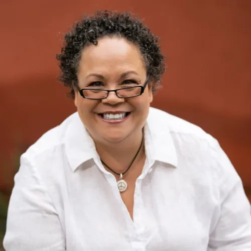Julie Lythcott-Haims smiles at the camera, wearing a white shirt and glasses.
