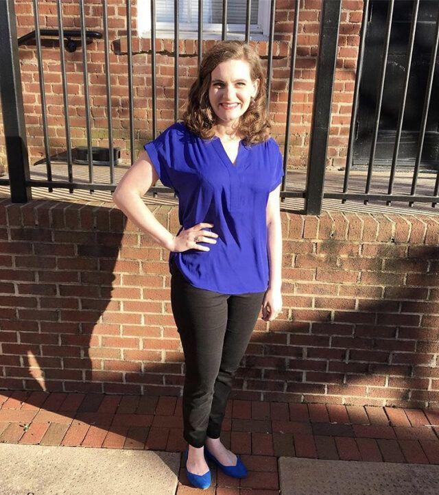 Rachel smiling and posing in front of a brick wall