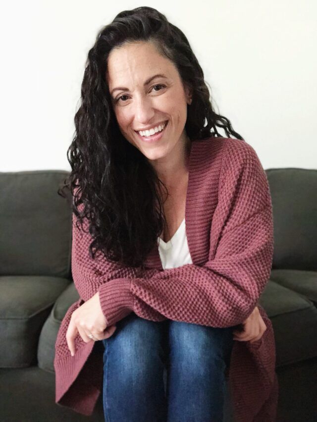 Nikki Reiland in a pink sweater sitting on a couch smiling