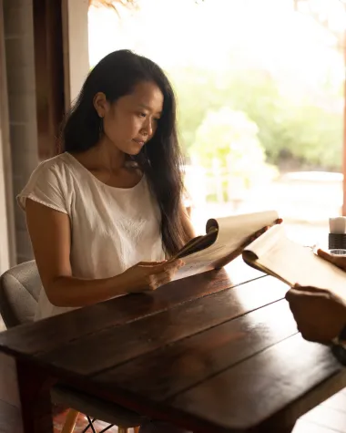 Woman sitting at a wooden table reading a paper menu.