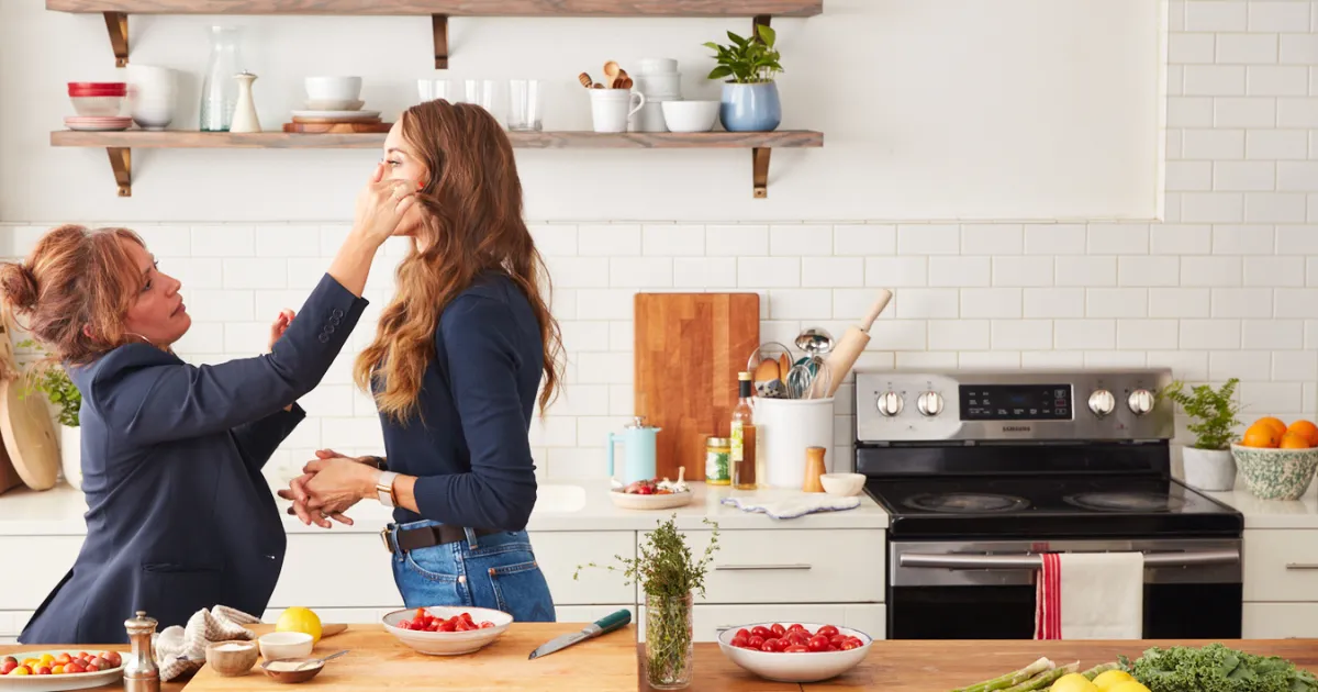 A behind the scenes photo of The New Whole30 showing Vanessa Vazquez facing Melissa Urban, fixing her hair, both standing in a kitchen