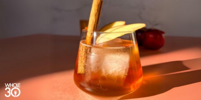 Cinnamon Apple Spice Mocktail in the sunlight in a clear glass with a cinnamon stick and apples to garnish.