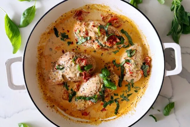 Whole30 Marry Me Chicken in white dish with basil leaf on a marble countertop