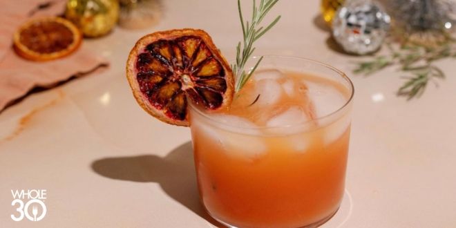 Sparkling Rosemary Citrus Mocktail on a marble surface, garnished with a sprig of rosemary and a dried blood orange in a small clear glass. 