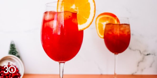 Whole30 Pomcran Mocktail displayed in two tall wine glasses, garnished with a slice of orange on the glass. 