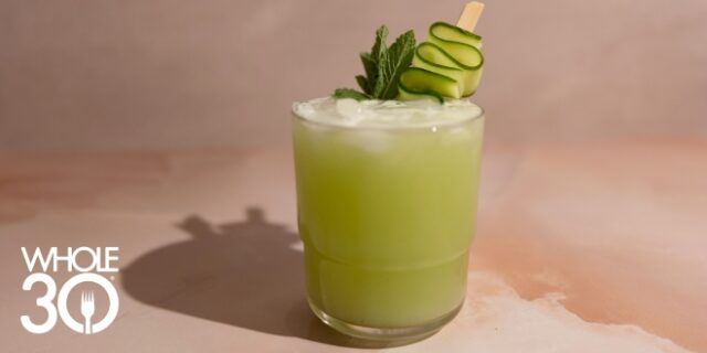 A bright green mocktail with a wavy cucumber ribbon garnish