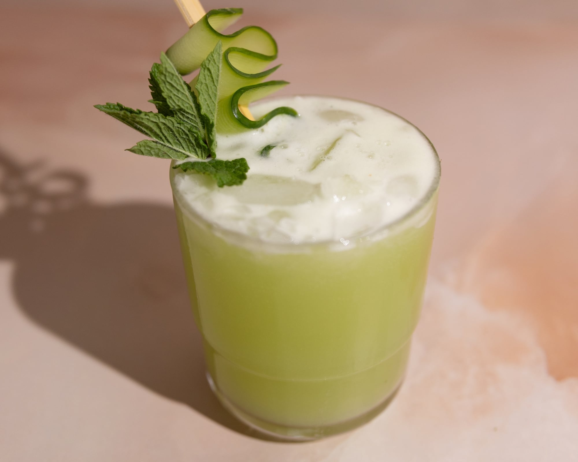 A bright green mocktail with a wavy cucumber ribbon garnish