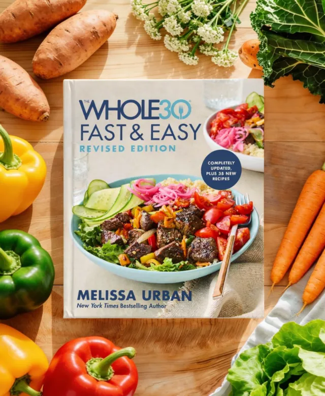 The Whole30 Fast and Easy Revised book laid on a wood countertop surrounded by fresh vegetables