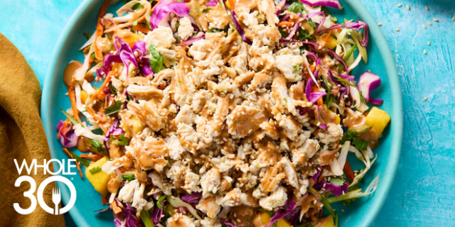 Thai-Inspired Chicken Salad with Ginger Dressing on a bright teal background with two small brown bowls containing sauce and sesame seeds
