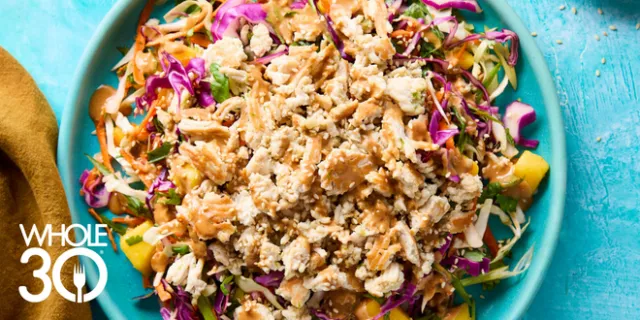 Thai-Inspired Chicken Salad with Ginger Dressing on a bright teal background with two small brown bowls containing sauce and sesame seeds