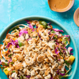 Thai-Inspired Chicken Salad with Ginger Dressing on a bright teal background with two small brown bowls containing sauce and sesame seeds
