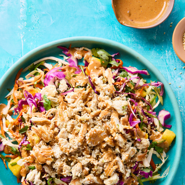 Thai-Inspired Chicken Salad with Ginger Dressing on a bright teal background with two small brown bowls containing sauce and sesame seeds