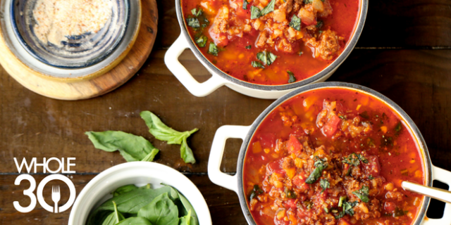 Hearty red stuffed pepper soup in two white ramekins, topped with fresh green herbs on wooden background