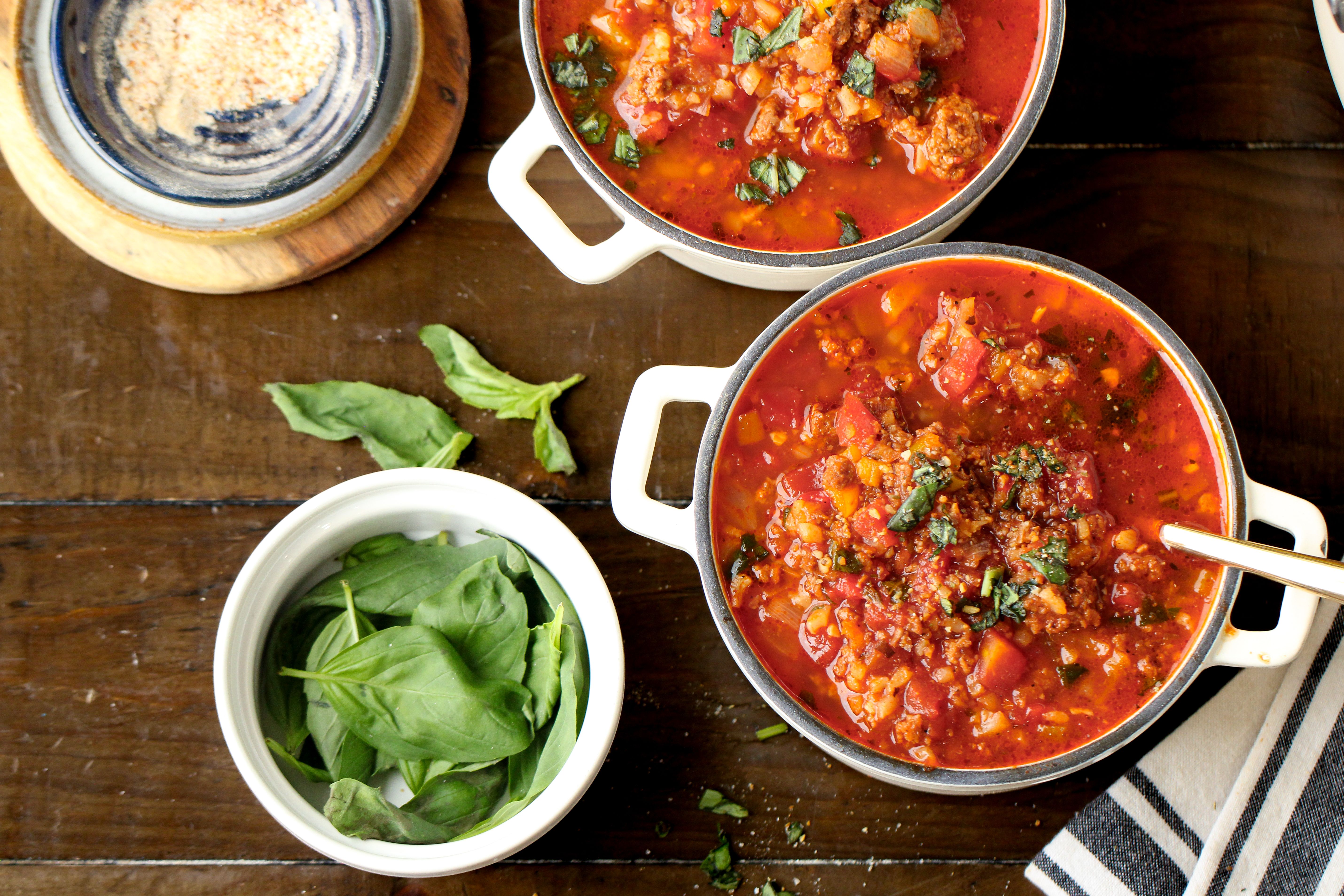 Hearty red stuffed pepper soup in two white ramekins, topped with fresh green herbs on wooden background